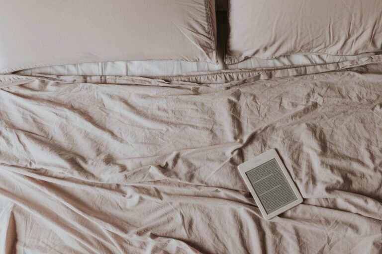 Kindle e-reader on soft white bed sheets, ready for a cozy reading session.