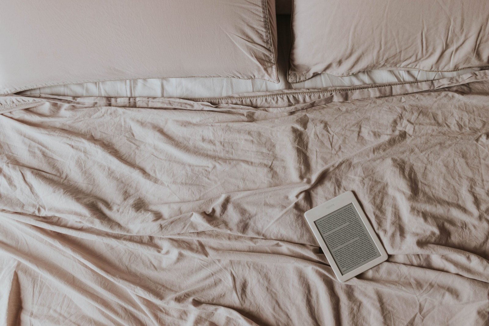 Kindle e-reader on soft white bed sheets, ready for a cozy reading session.